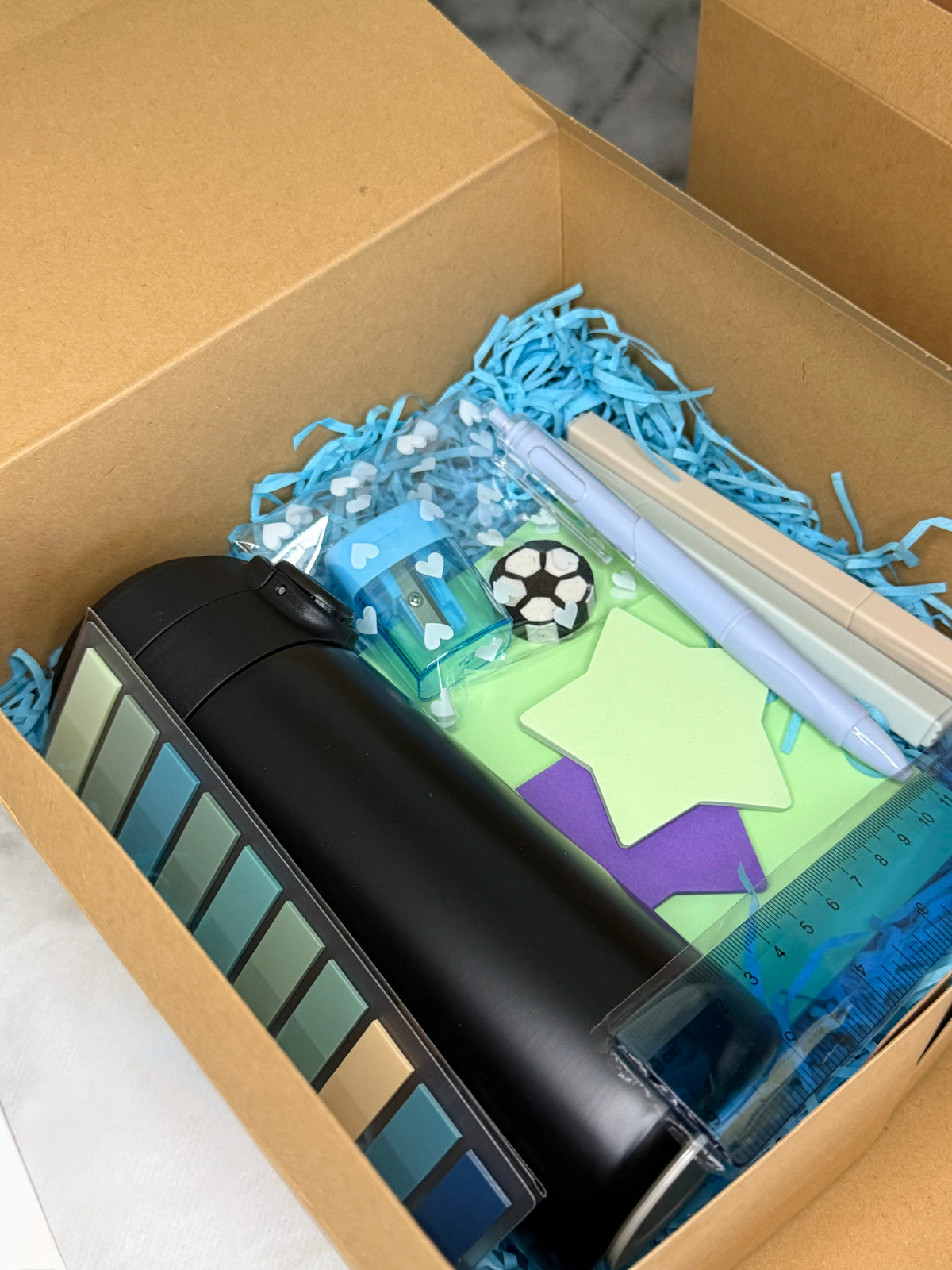Boys' Back to School football-themed stationery gift set in a kraft box with blue shredded paper, black thermos, football eraser, ruler, sticky notes and pens